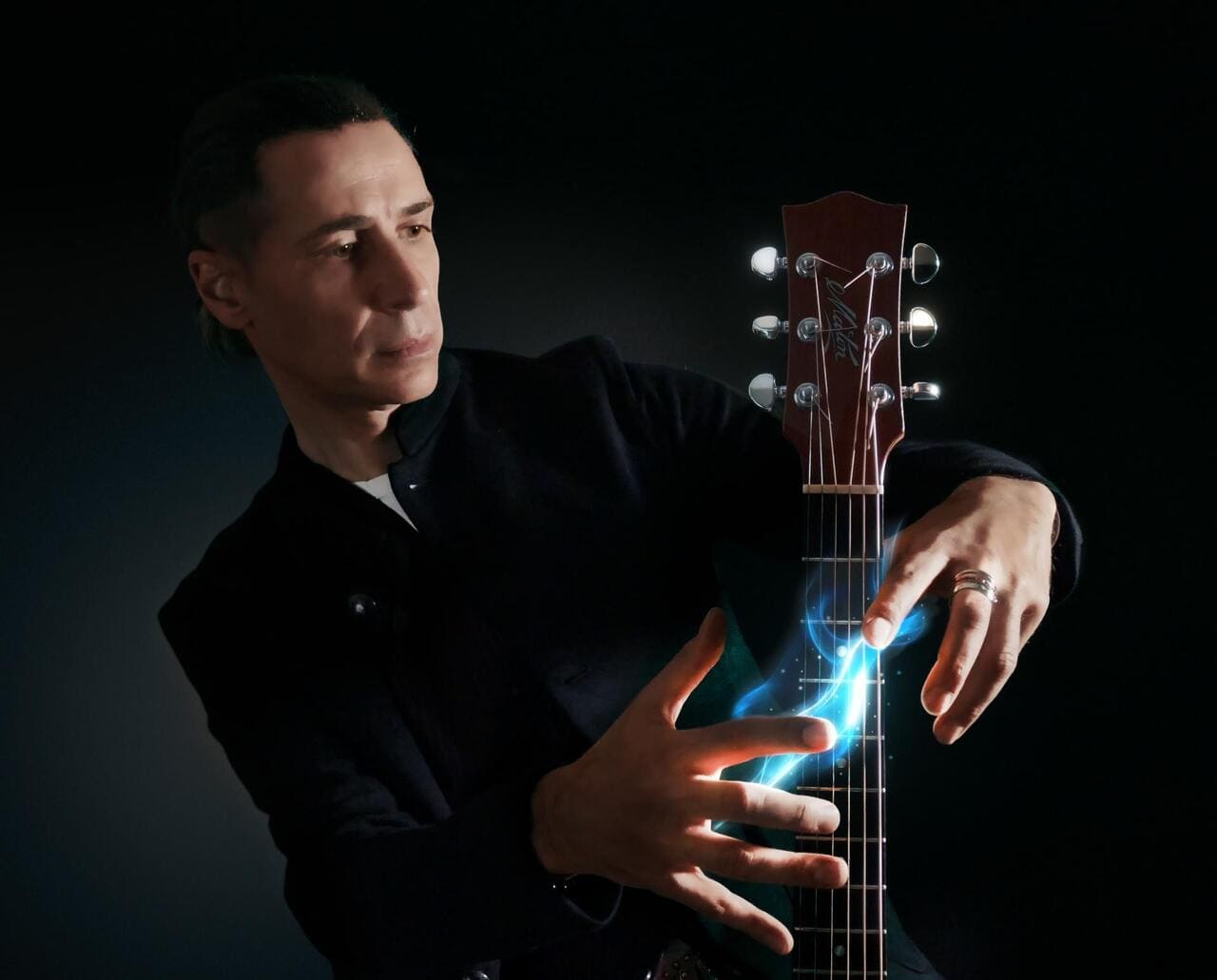 Max Spurio suona la chitarra durante il recital “Note di Viaggio”, con effetti luminosi sulle corde, in un contesto scenico scuro.